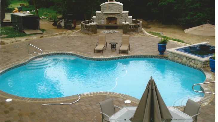 A pool surrounded by brick with a fireplace in the back