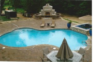 A brick landscape surrounding a pool with a hot tub, and stylized brick fireplace