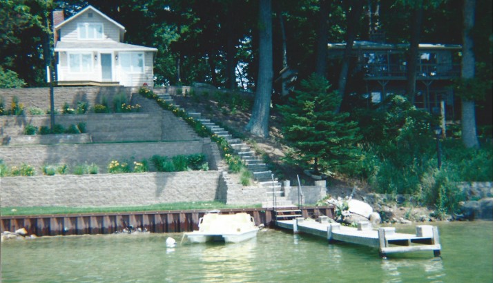A lakeside house that has a series of brick walls leading up a hill with brick stairs