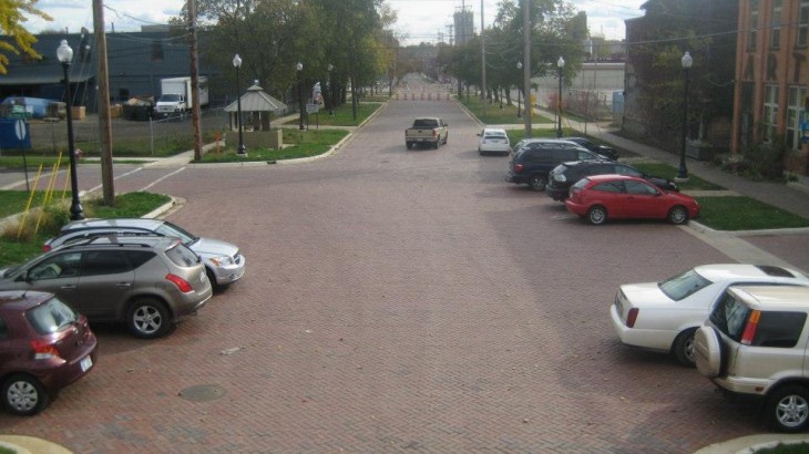 A brick road made by Brick Pavers Construction with cars parked along the street of a downtown area