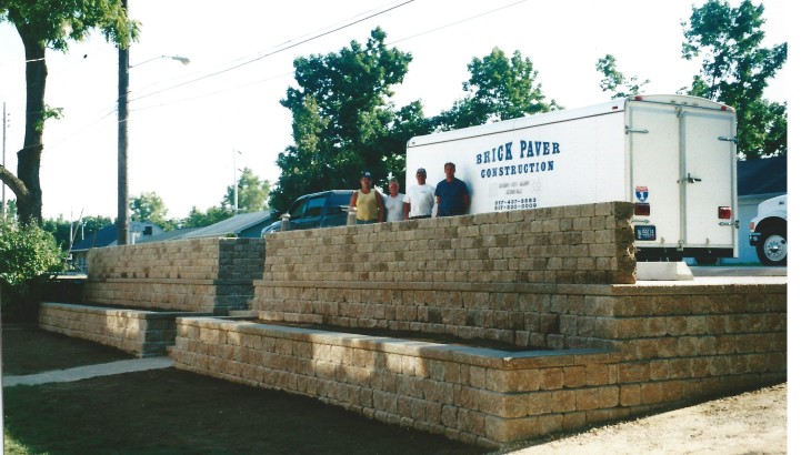 Brick Paver Construction staff standing behind a brick wall next to their trailer which features their logo