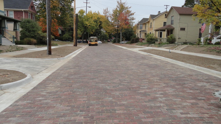 A finished brick road that runs through a subdivision with houses on both sides