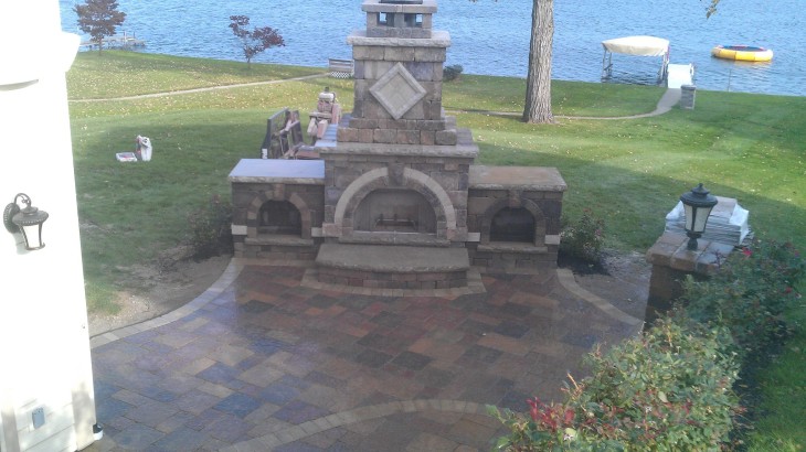 An outdoor brick fireplace with a brick pathway leading up to it with a lakeside backdrop