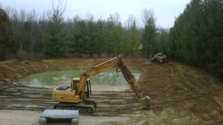 Brick Pavers Construction operating excavators to dig out a man made pond in a wooded area