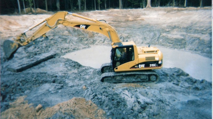Brick Paver's Construction operating a Cat Excavator to dig out a man made pond in a wooded area