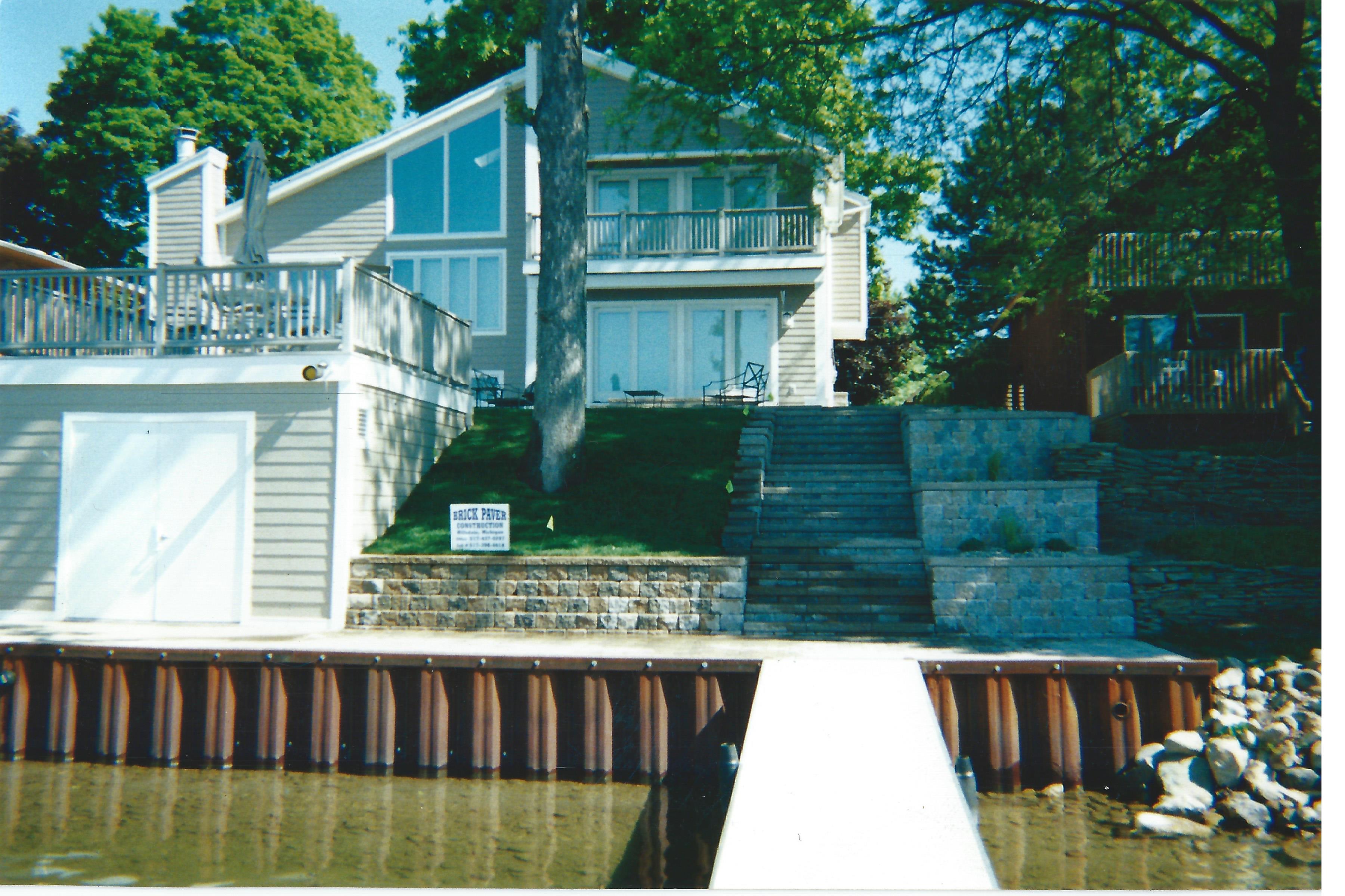 A house perched high on a lakeside with layers of retaining walls made by Brick Pavers Construction