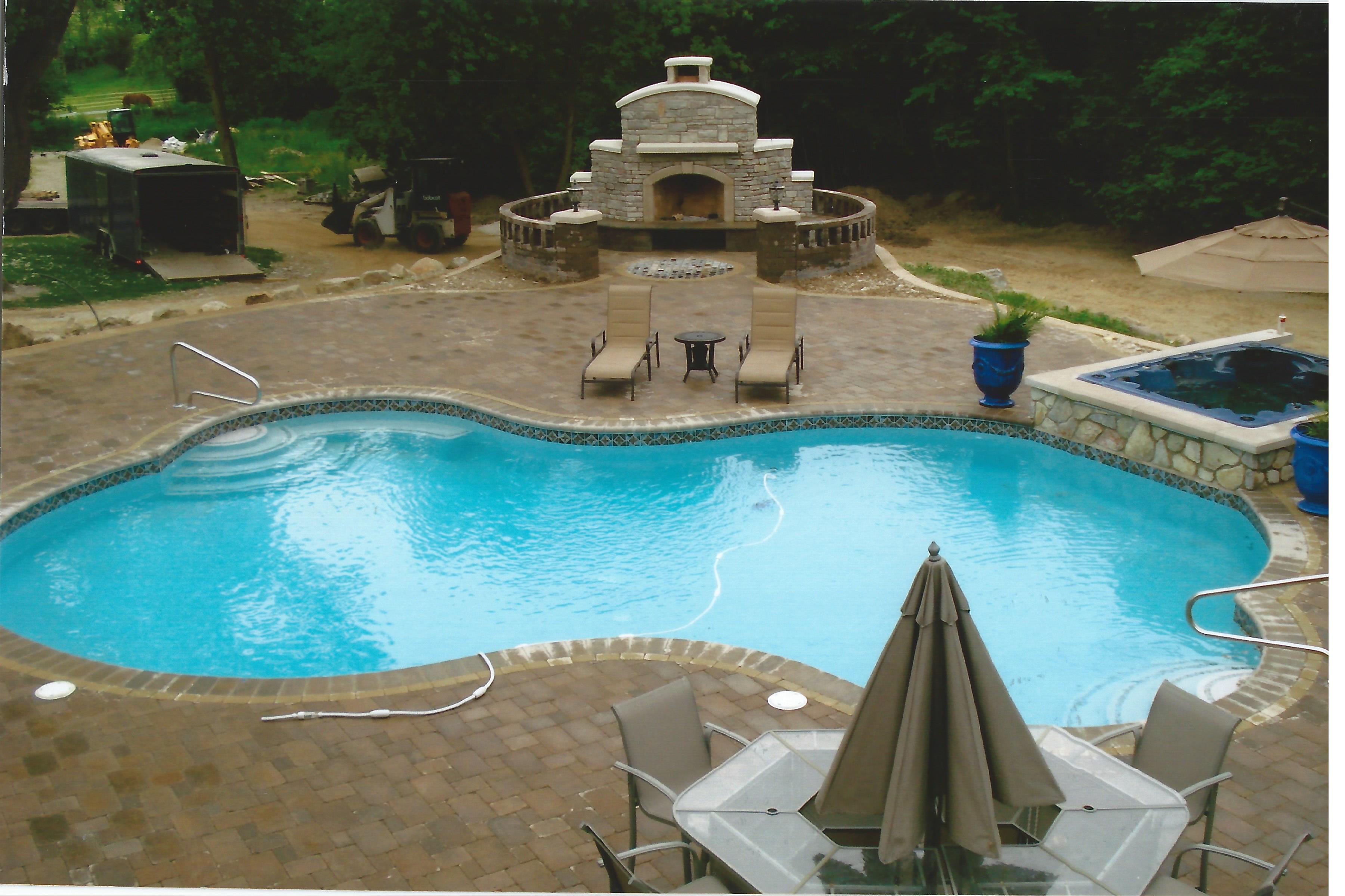 A pool surrounded by brick with a fireplace in the back