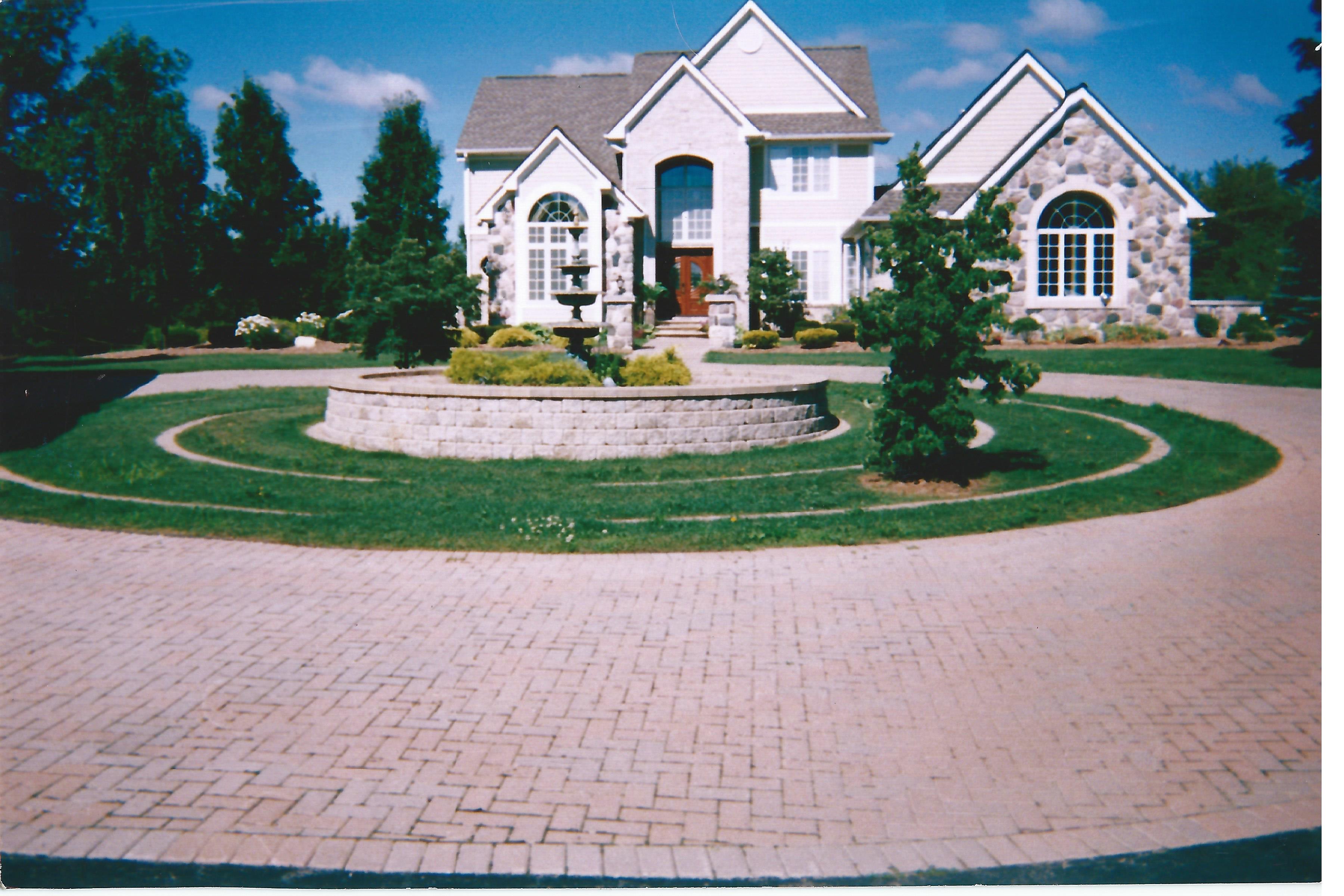 A circle driveway outside of a house made out of brick with a fountain in the middle