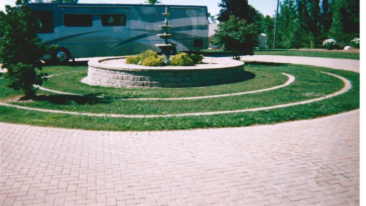A brick pathway that circles landscape with a fountain in the middle