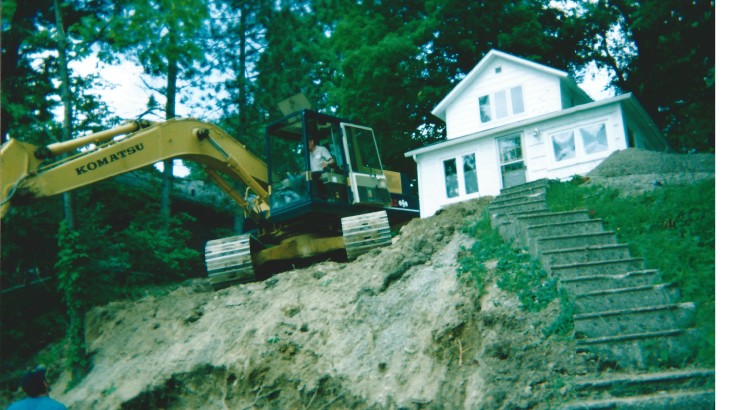 Stone steps leading up to a house with a Komatsu Excavator digging up the Earth