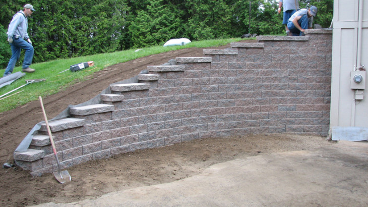 A brick retaining wall with members of Brick Pavers Construction placing down bricks