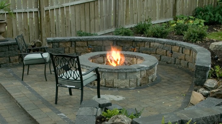 Chairs positioned outside a Fire pit ring made out of brick with brick ground
